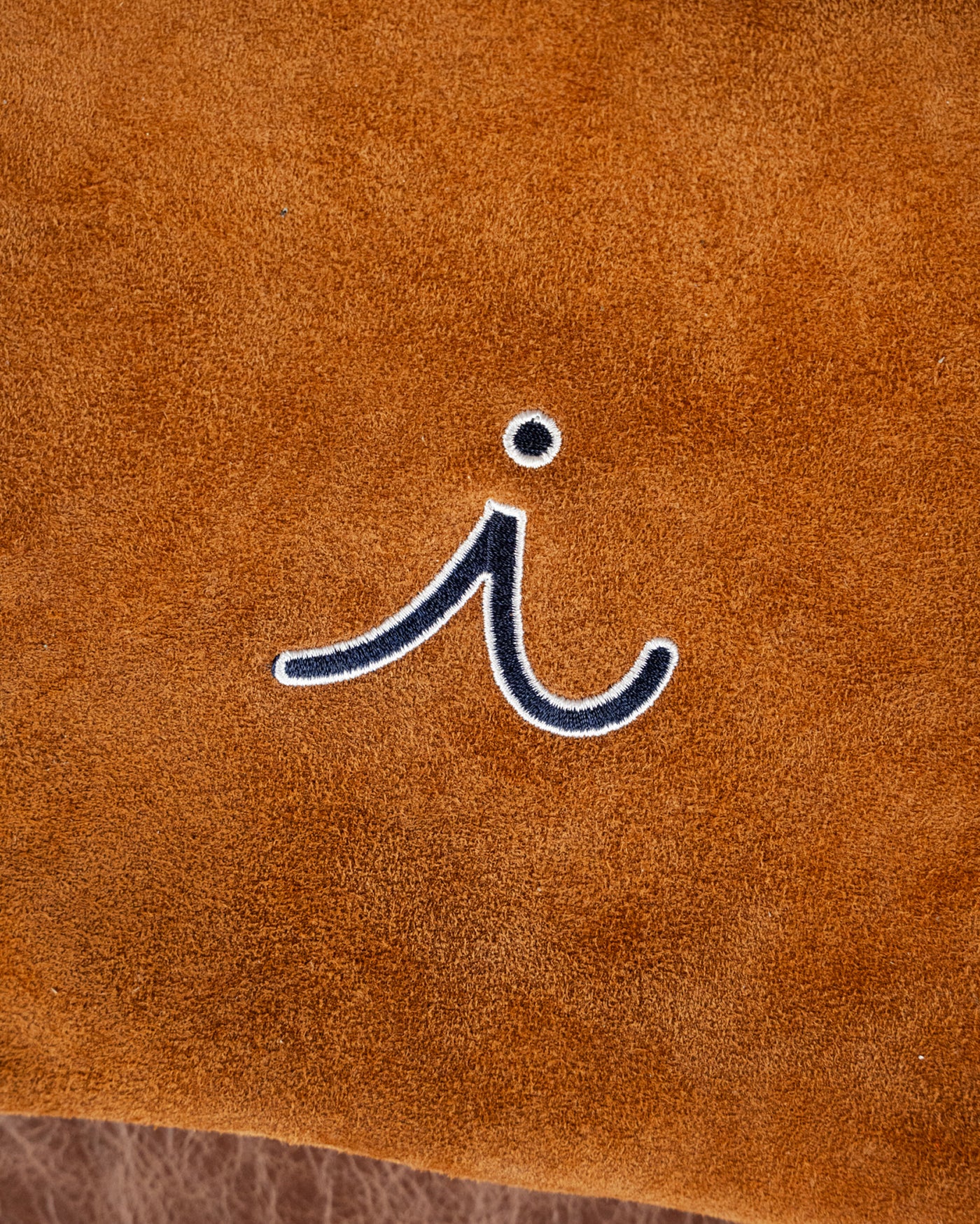 Detail of the embroidered i on the caramel suede Velora clutch