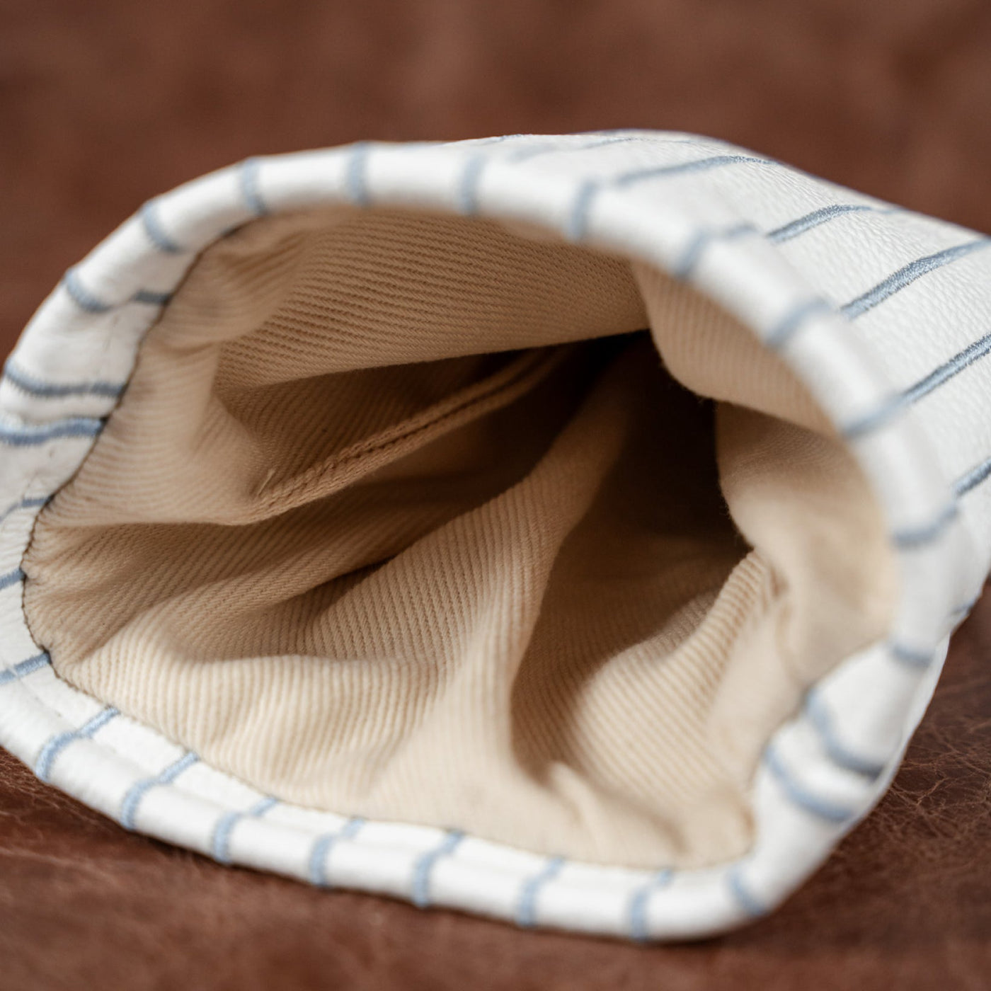 Close-up of a fabric pouch or sleeve with a beige interior and a white exterior featuring thin blue stripes, set against a brown textured background.